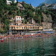 Blick vom Wasser aus auf die Küste mit Gebäuden und begrüntem Fels im Hintergrund - Übernachtung während einer individuellen Wanderung in Italien