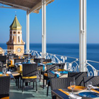 Blick von einer Terrasse mit vielen Sitzgruppen auf das offene Meer, im Hintergrund ein Kirchturm - Übernachtung während einer individuellen Wanderung in Italien