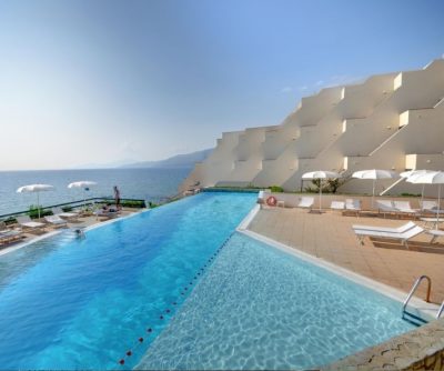 Blick auf einen großen Pool mit Liegestühlen und Sonnenschirmen, dahinter das Meer und andere Wohnungen des Hauses - Übernachtung während der individuellen Wanderung in Süd-Italien