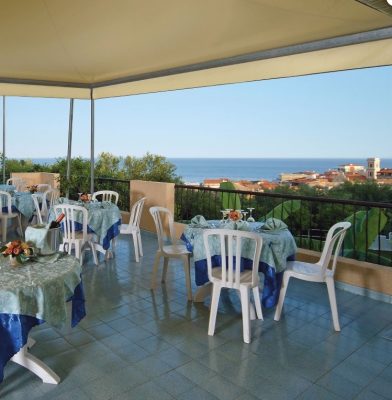 Eine überdachte Terrasse mit Tischgruppen und Blick auf andere Häuser und das blaue Meer - Übernachtung während der individuellen Wanderung in Süd-Italien 