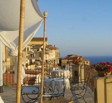 Eine Terrasse mit Sonnensegel, eine Tischgruppe, dahinter andere Häuser, das Meer und der blaue Himmel - Übernachtung während der individuellen Wanderung in Süd-Italien