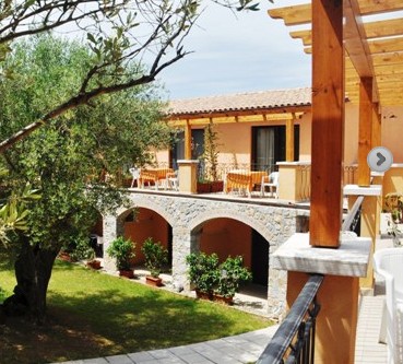 Blick vom Balkon eines orangenen Hauses in den Garten mit großem Baum und Wiese und auf die anderen Balkone des Gebäudes - Übernachtung während der individuellen Wanderung in Süd-Italien