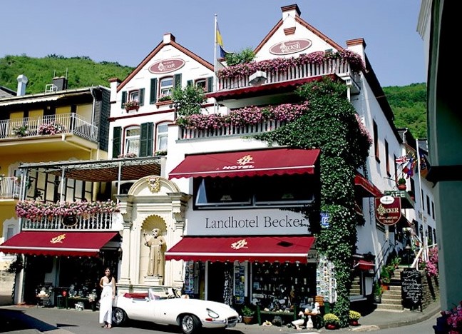 Hotel mit weißer Fassade und roten Markisen vor blauem Himmel - Überanchtung im Landhotel Becker, Kamp-Bornhofen auf einer individuellen Wanderung am Rhein