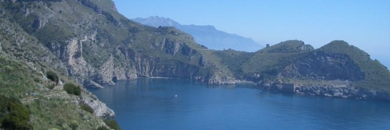 Blick über das blaue Meer auf einen begrünten Bergkamm, im Hintergrund weitere Berge - gesehen auf einer individuellen Wanderung in Italien