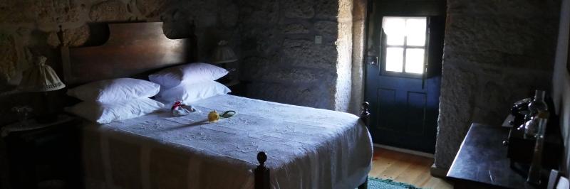 Ein Doppelbett in einem Schlafzimmer mit steinernen Fassaden und einer Tür in den Außenbereich - gesehen auf der individuellen Wanderung in Nord-Portugal