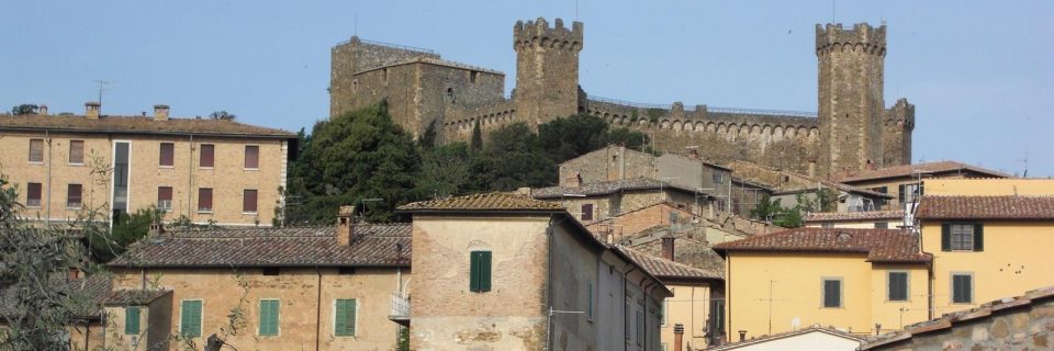 Zahlreiche helle steinerne Hausfassaden, im Hintergrund ein Burgturm - gesehen auf einer individuellen Wanderung in der Toskana